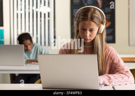 Diversi compagni di classe adolescenti con cuffie, donna in maglione rosa che usa un laptop, uomo che scrive su un quaderno Foto Stock