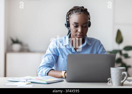 Giovane operatore telefonico nero femmina in cuffia che lavora con il computer portatile in ufficio Foto Stock