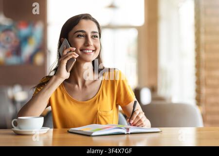 Giovane donna allegra che ha conversazione con il datore di lavoro sul telefono Foto Stock