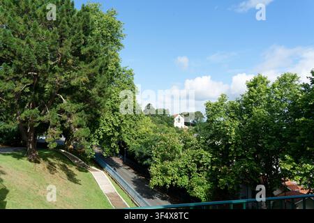 Parco moresco con alberi rigogliosi, scale bianche, una strada e edifici sotto un cielo blu Foto Stock