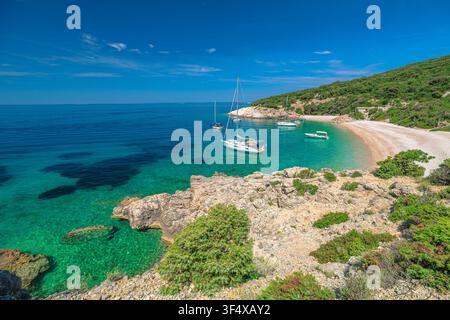 Mar Adriatico alla spiaggia di Sveti Ivan sull'isola di Cres, Croazia, che mostra acqua turchese che riflette le colline verdi vibranti e diverse barche ancorate nelle vicinanze Foto Stock
