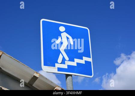 Segnale quadrato blu con figura bianca che scende le scale contro il cielo blu passaggio sotterraneo Foto Stock