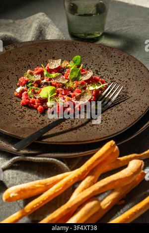 Piatto di tartara di manzo gourmet con tartufo nero, verdure e una forchetta su un piatto scuro Foto Stock