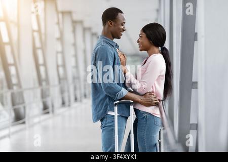 Amando l'uomo afroamericano e la donna coccolarsi nel terminal dell'aeroporto Prima del volo Foto Stock