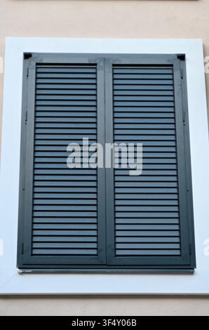 Una finestra chiusa con persiane in legno su una facciata di edificio in una luce neutra, che offre una vista frontale di architettura moderna con elementi di design puliti. I toni bianco e grigio. Foto Stock