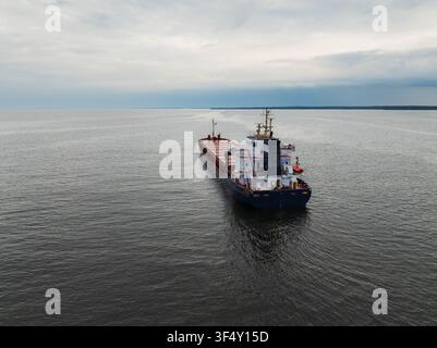 Vista aerea di poppa di una nave da carico che naviga nel Mar Baltico vicino alla costa estone con un risveglio dell'acqua sotto un cielo nuvoloso drammatico. Foto Stock