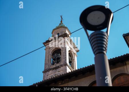 Bergamo, Italia - 16 giugno 2026: Scatto architettonico ad angolazione bassa di un antico campanile in pietra contro un cielo blu terso, incorniciato da un moderno sfocato Foto Stock