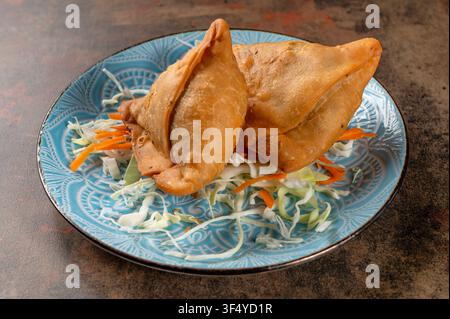 Samosas indiani autentici al pollo, realizzati con sfoglia triangolare croccante di grano, ripieni di pollo tritato leggermente speziato, serviti con guarnizione di cavolo fresco Foto Stock