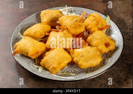 Paneer Pakora servito su un piatto di ceramica con cavolo e carota grattugiati. Antipasto tradizionale indiano a base di formaggio fresco fritto rivestito con farina di ceci b Foto Stock