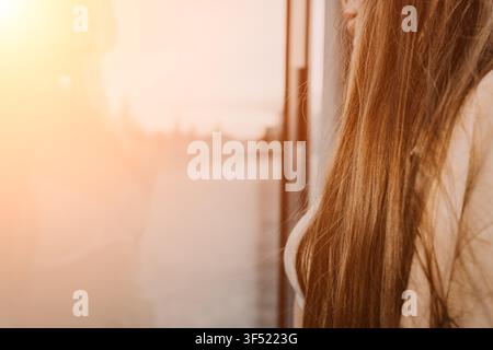 Capelli di donna al tramonto primo piano di lunghi capelli biondi lisci che brillano nella luce dorata di un tramonto vicino a una finestra Foto Stock