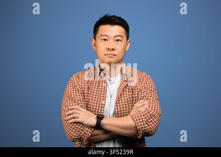 Uomo asiatico sicuro di sé con le braccia incrociate su sfondo blu, concetto aziendale Foto Stock