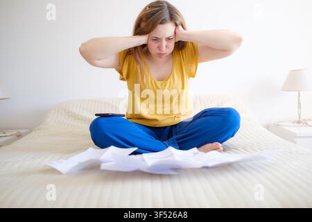 Donna che si sente sopraffatta dall'ansia finanziaria, seduta con le bollette su un letto Foto Stock