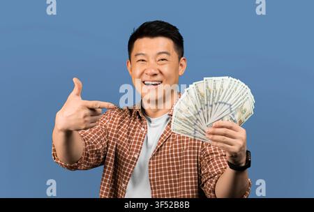 Uomo asiatico felice che mostra denaro con entusiasmo, sfondo studio, concetto aziendale Foto Stock