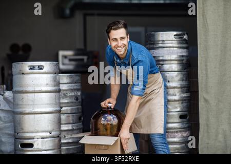Giovane uomo caucasico sorridente che lavora in panetteria, sposta una cupola per torte in cucina Foto Stock