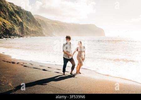 Giovane coppia che si tiene per mano su una spiaggia di sabbia nera Foto Stock