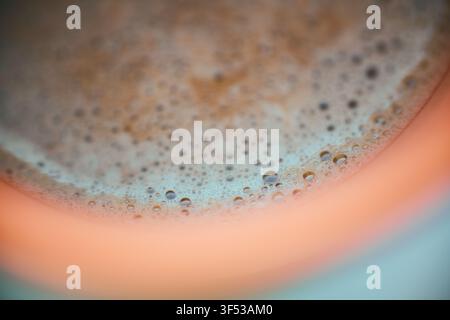 Primo piano estremo di una ricca crema di caffè marrone con piccole bolle che galleggiano in superficie all'interno di una tazza di ceramica, evidenziando la texture liscia e il tono caldo Foto Stock