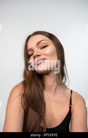 Giovane donna che posa guardando la fotocamera con sicurezza ed espressione rilassata, capelli lunghi naturali e pelle luminosa Foto Stock