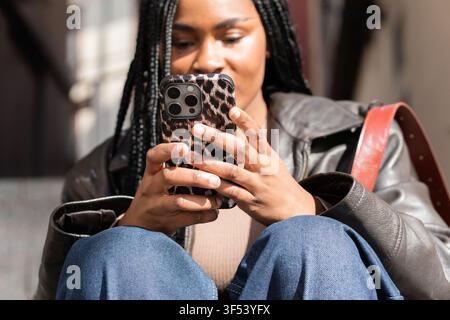 Studente sorridente che usa il telefono cellulare e indossa un'elegante custodia con stampa animale Foto Stock