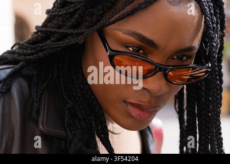 Ritratto di una giovane donna afroamericana alla moda con lunghe trecce e occhiali da sole Foto Stock
