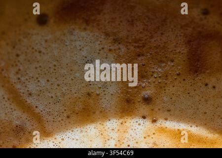 Dettaglio macro in primo piano della crema di caffè espresso fresco che mostra una texture intricata di schiuma marrone dorata e minuscole bolle d'aria sulla bevanda calda Foto Stock