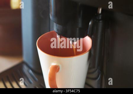 Prima vista di caffè espresso caldo appena preparato versato dalle doppie ugelle di una moderna macchina da caffè automatica in una tazza di ceramica colorata. Foto Stock