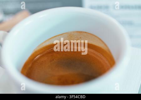 Prima vista di caffè espresso appena preparato con ricca crema dorata all'interno di una tazza di ceramica bianca pulita su una superficie di tavolo. Foto Stock
