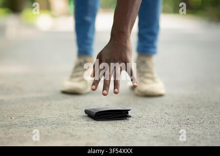 Vista ravvicinata del ragazzo nero che raccoglie il portafoglio perso sulla strada della città Foto Stock