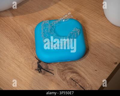 Allineatori dentali in plastica trasparente appoggiati su una custodia blu posizionata su una superficie di legno in una vista ravvicinata. Foto Stock