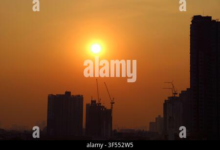 Sole luminoso che splende su un cielo arancione dorato sopra gruppi di grattacieli Foto Stock