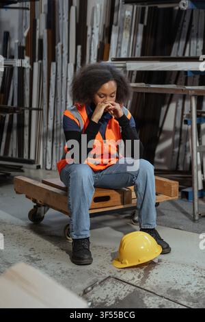 Una donna è seduta su un carrello di legno in una fabbrica, sembra stressata e stanca dopo aver completato il suo turno. La stanchezza è visibile sul suo viso. Foto Stock