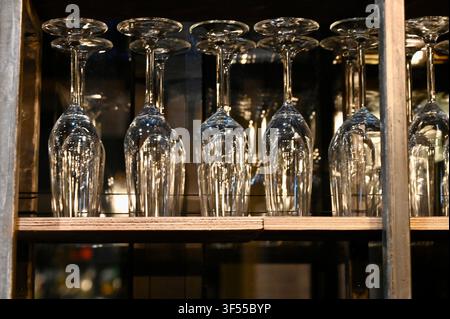 Prima vista di bicchieri da vino in cristallo trasparente appesi a testa in giù su una mensola di legno in un bar ristorante o in un armadio. Foto Stock