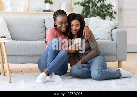 Due allegre sorelle afroamericane che controllano i social media sullo smartphone Foto Stock