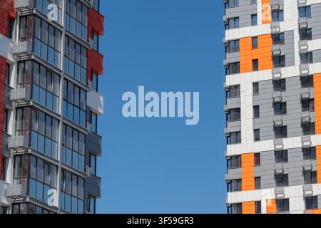 Edifici alti con facciate rosse, arancioni e grigie sorprendenti toccano il cielo blu chiaro. La luce del sole si riflette sulle finestre di vetro, contribuendo alla città vivace Foto Stock