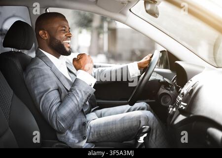 Giovane uomo d'affari nero emotivo che guida dopo un incontro d'affari riuscito Foto Stock