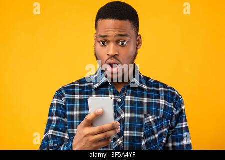 Un ragazzo scioccato che guarda lo smartphone che legge notizie scioccanti in Studio Foto Stock
