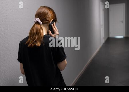 Donna che parla al telefono cercando la privacy in un corridoio Foto Stock