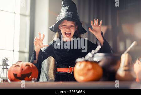 Bambino allegro vestito con un classico costume da strega che fa facce spaventose giocose mentre si gode le feste di Halloween circondato da zucche intagliate e ho Foto Stock