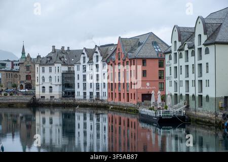 Gli edifici storici colorati del lungomare di Ålesund si riflettono nelle acque calme del canale in una giornata nuvolosa e atmosferica, perfetti per uso turistico e editoriale. Foto Stock