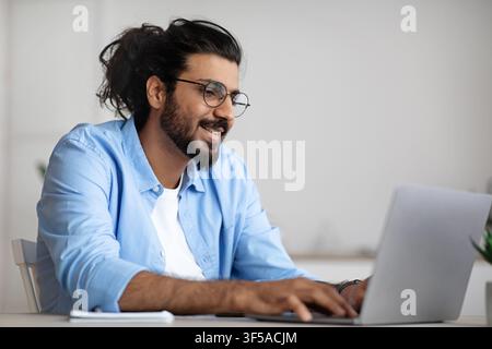 Guy, responsabile IT indiano impegnato a lavorare su notebook presso Workplace In ufficio Foto Stock