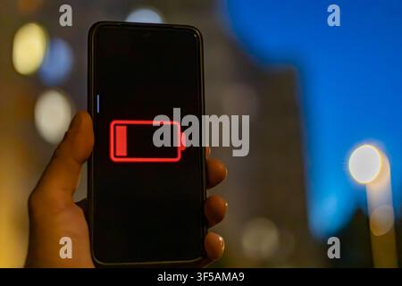Primo piano di una mano che tiene uno smartphone con icona di batteria scarica di notte Foto Stock