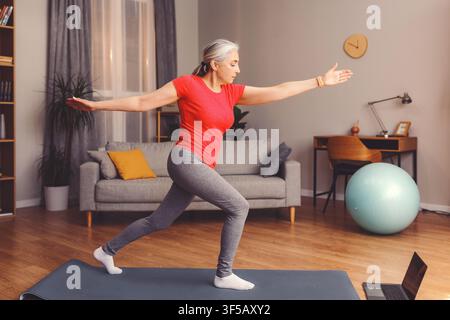 Donna caucasica anziana che pratica yoga a casa su un tappetino, concetto di stile di vita concentrato e attivo Foto Stock
