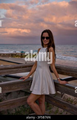 Donna in abito estivo bianco in piedi su una passeggiata al crepuscolo Foto Stock