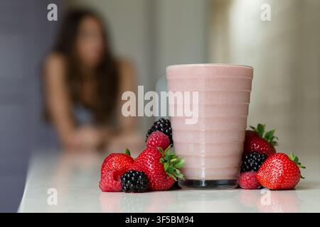 Un frullato di bacche e bacche fresche miste sono disposti in primo piano con una donna fuori fuoco sullo sfondo l'11 giugno 2016. Foto Stock