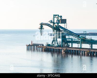 Molo del porto di Ventspils con trasportatore verdeazzurro e gru per il caricamento di merci alla rinfusa Foto Stock