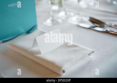 Biglietto da posto bianco vuoto piegato su un tovagliolo ordinatamente piegato, apparecchiatura per una ricevimento di nozze o una cena formale di banchetto, elegante preparazione del banchetto Foto Stock