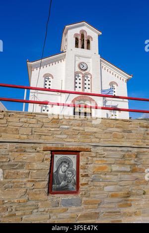 Chiesa di Agios Filippos a Batsi con torre dell’orologio e icona religiosa su un muro di pietra, Andros, Grecia Foto Stock
