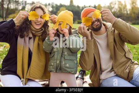 Famiglia sorridente che gioca con foglie gialle nel parco autunnale, volti allegri e divertimento Foto Stock