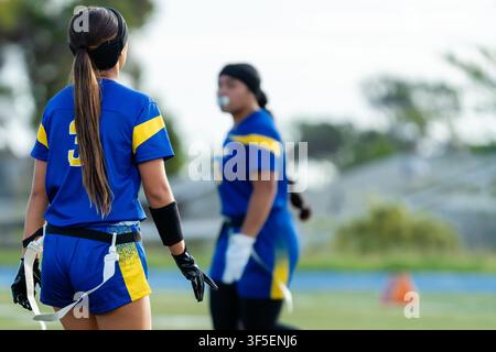 Vista posteriore di una giocatrice di flag football numero 3 in piedi sul campo con una compagna di squadra sfocata sullo sfondo. Foto Stock