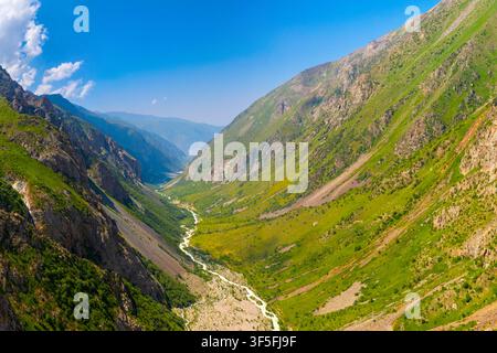 Una veduta aerea cattura una vasta valle montana con un fiume sinuoso e colline rigogliose e verdi. Il cielo blu brillante e le nuvole bianche esaltano la grandezza naturale. Foto Stock