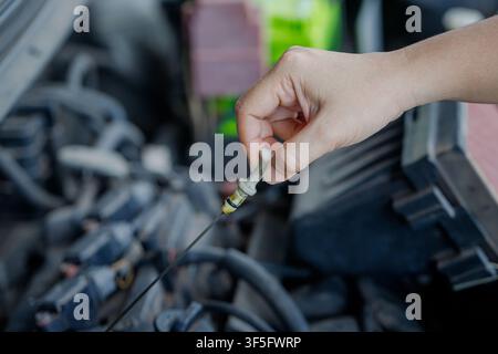 Primo piano di una mano di un meccanico che estrae la bacchetta del livello dell'olio motore per controllare il livello dell'olio, evidenziando la manutenzione del veicolo e la cura del motore in un ambiente di officina Foto Stock